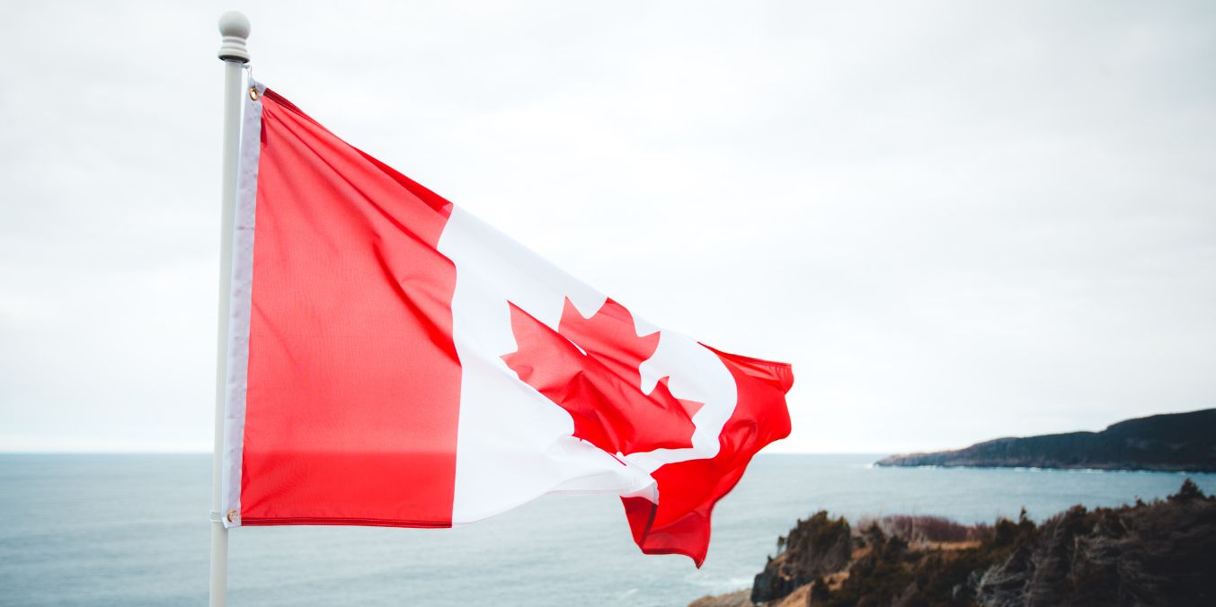 Canadian flag waving against a coastal backdrop, symbolizing the comparison of living costs across major cities in Canada