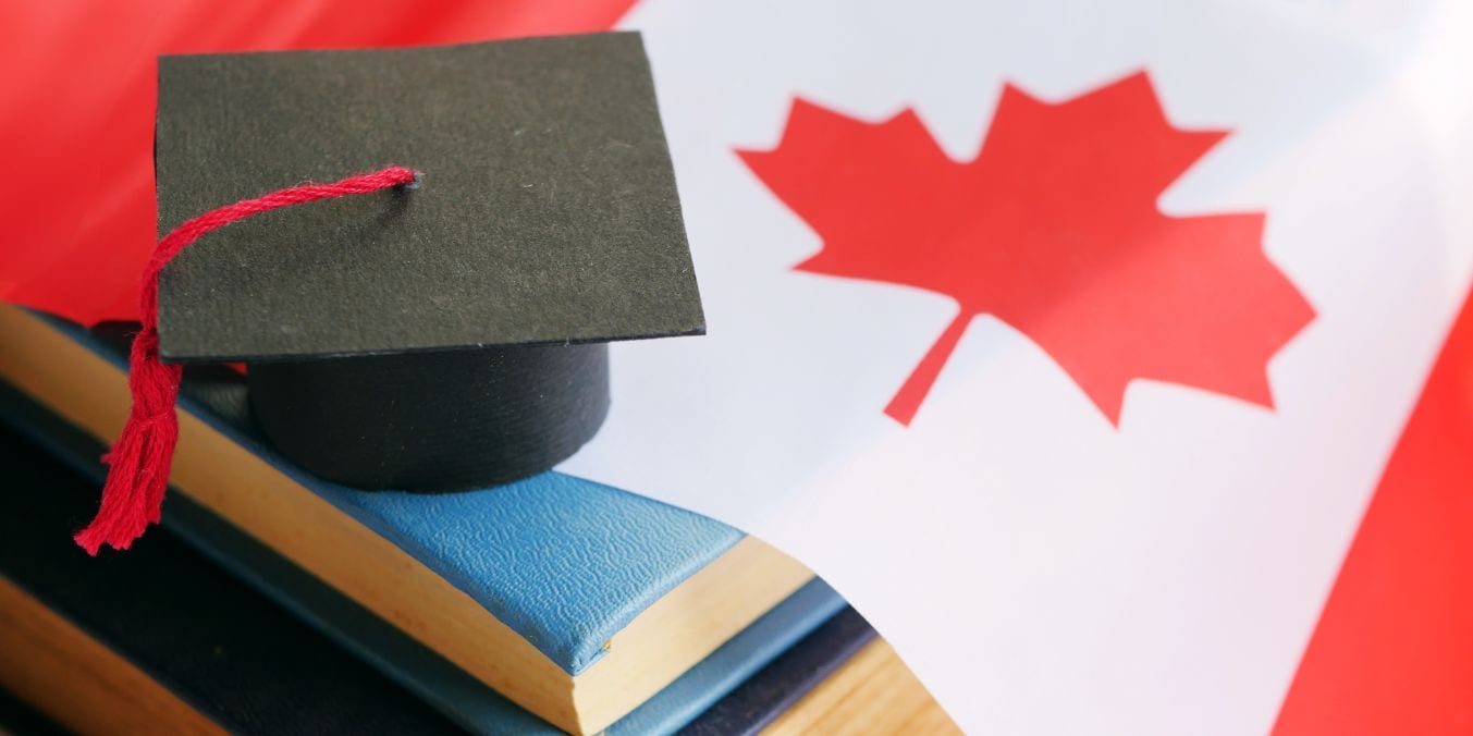 Graduation cap on books against a Canadian flag, symbolizing the accessible and inclusive education system in Canada for immigrants and diverse communities