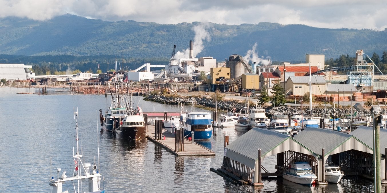 Boats docked at a marina with industrial buildings and forested mountains in the background in Port Alberni, showcasing it as one of the best places to live on Vancouver Island