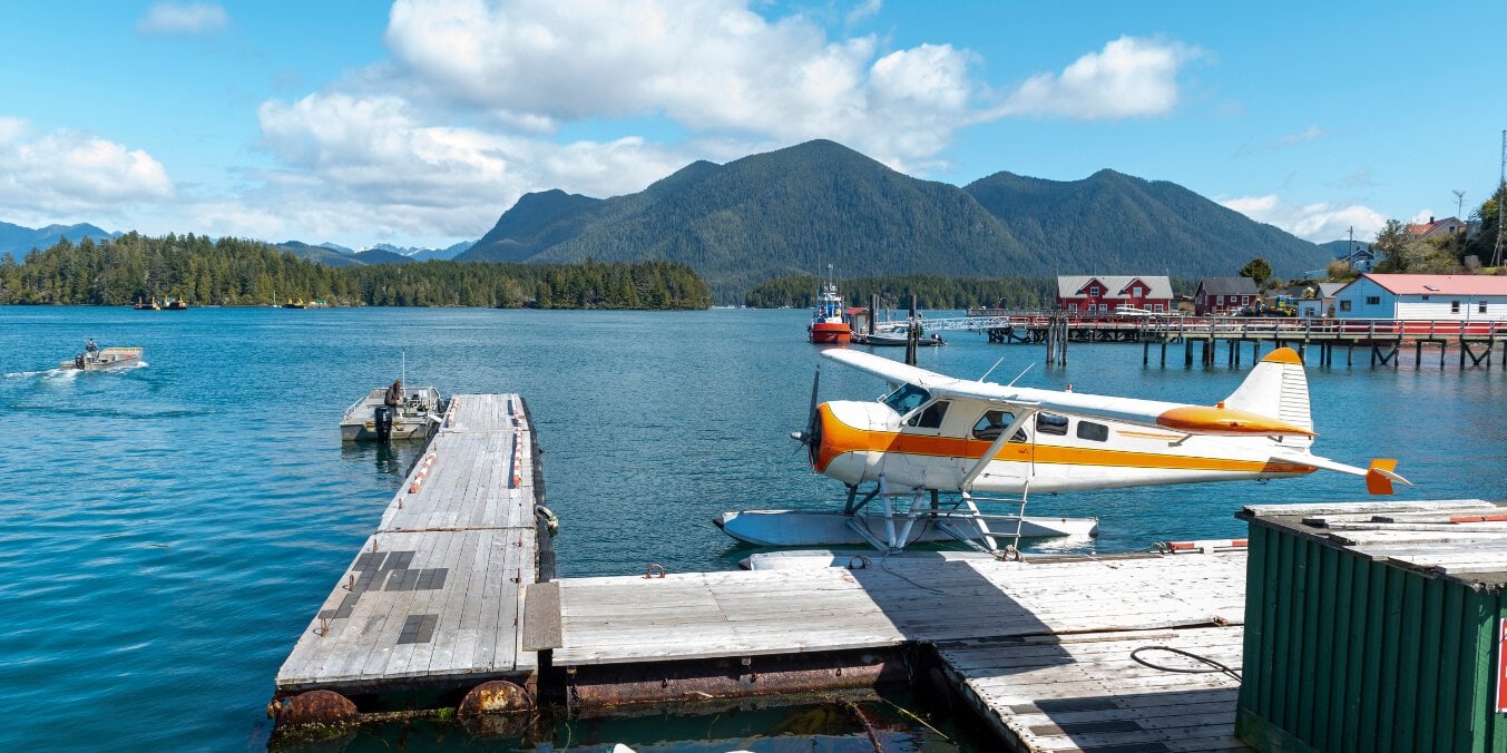 A seaplane docked at a pier with mountains and waterfront buildings in the background, highlighting Tofino as one of the best places to live on Vancouver Island