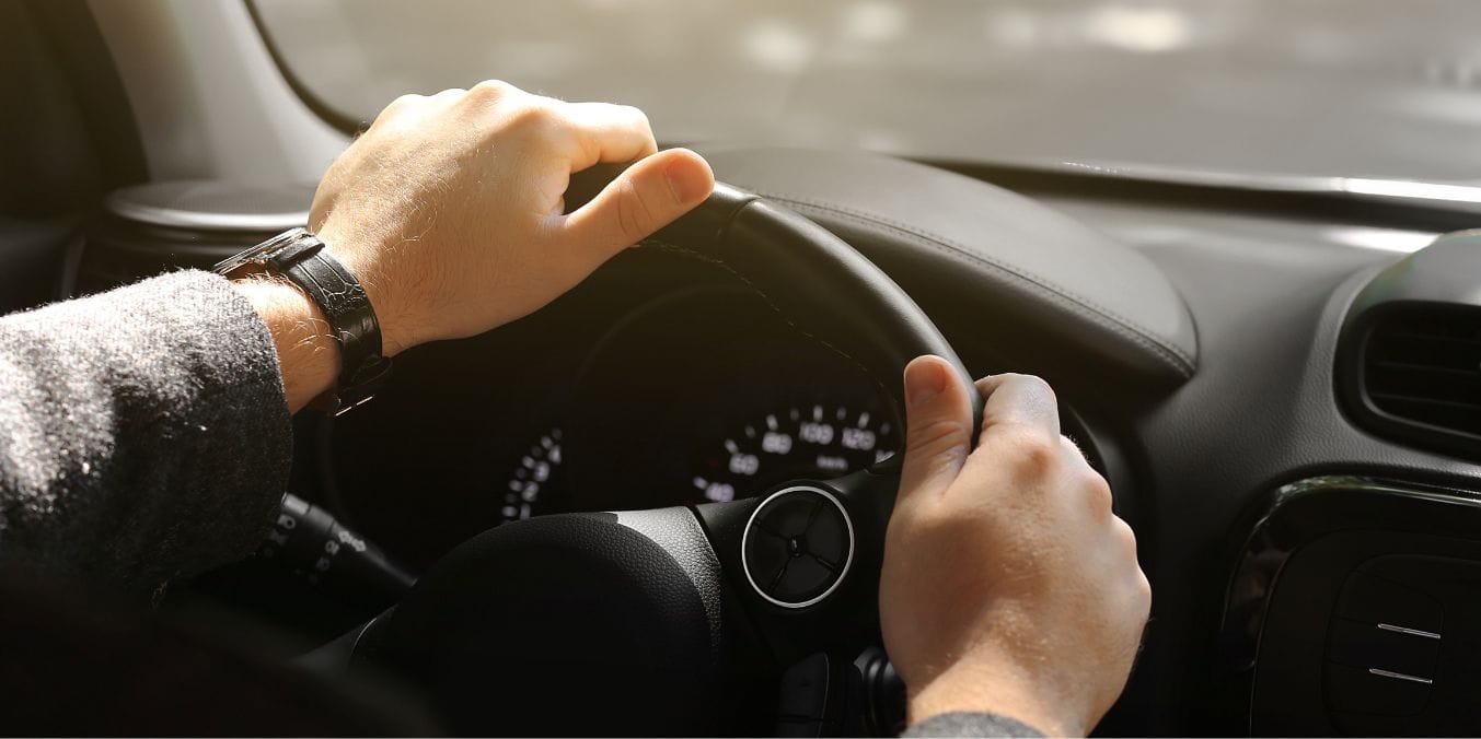 Close-up of a driver's hand steering a car in Vancouver, illustrating the personal vehicle costs related to fuel, insurance, and parking in 2024