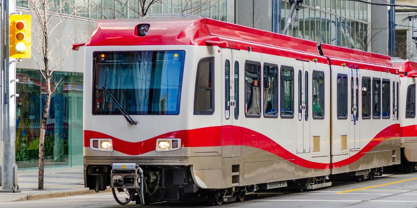 A red and white CTrain light rail vehicle travel down a street, highlighting the public transportation and commuting in Calgary vs Winnipeg.