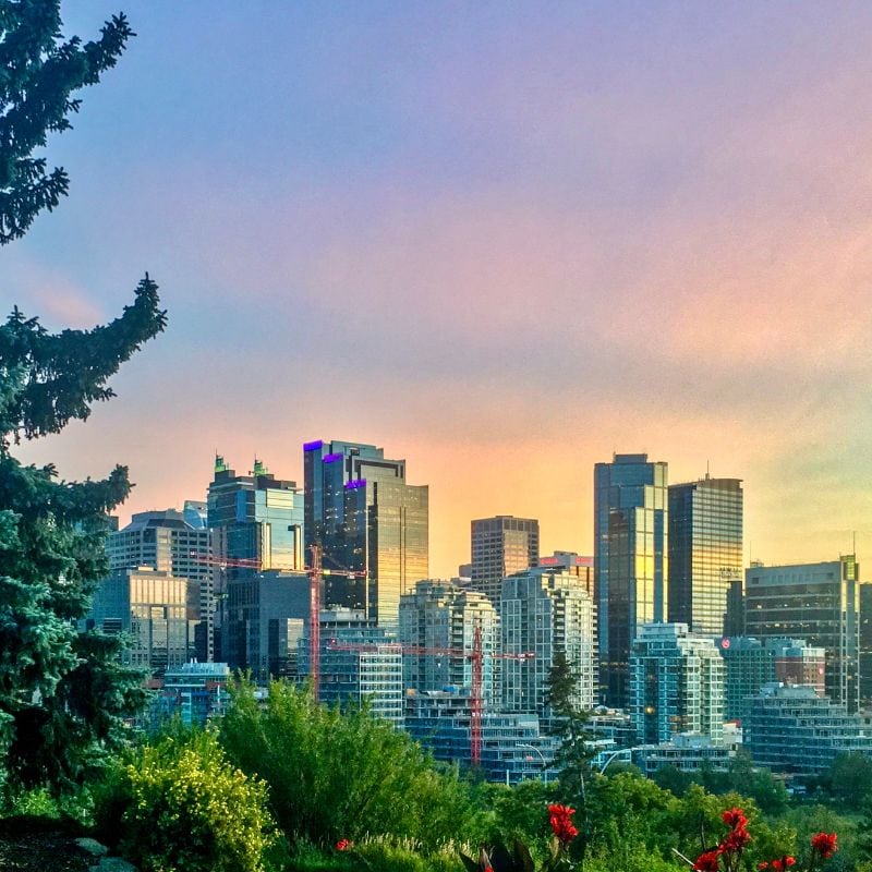 A panoramic view of the skyline at sunset, with towering skyscrapers bathed in warm orange and pink hues in the Calgary vs Winnipeg Canadian Cities.