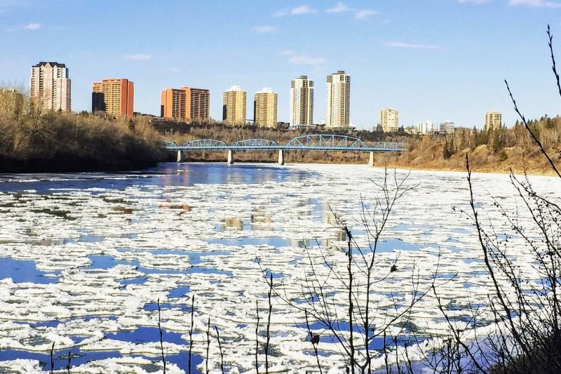 Edmonton skyline with a partially frozen river in the foreground, representing the city's vibrant arts scene and diverse economy in the Edmonton vs Vancouver.