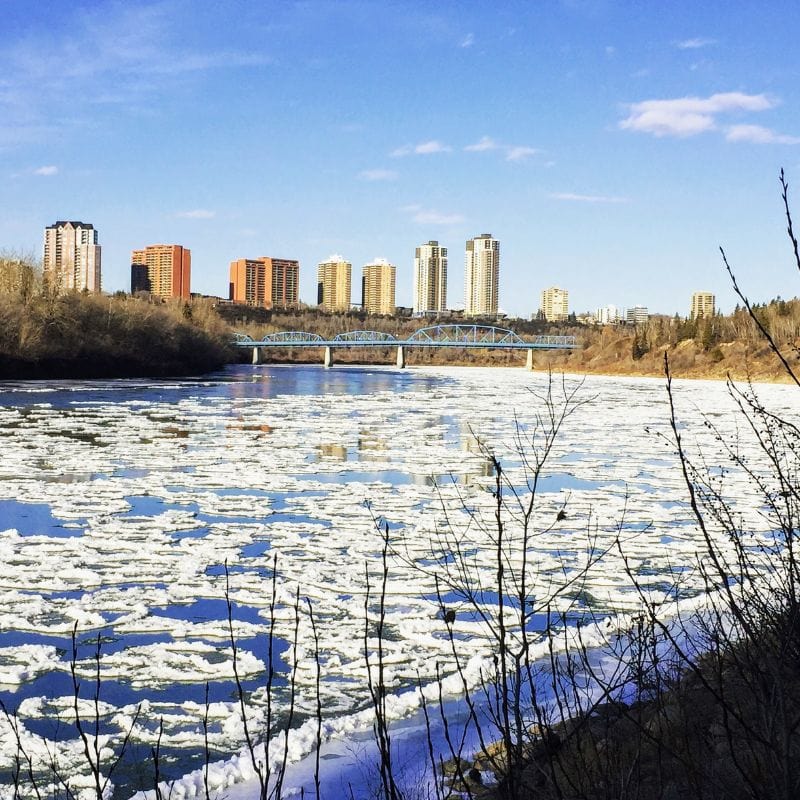 Edmonton skyline with a partially frozen river in the foreground, representing the city's vibrant arts scene and diverse economy in the Edmonton vs Vancouver.