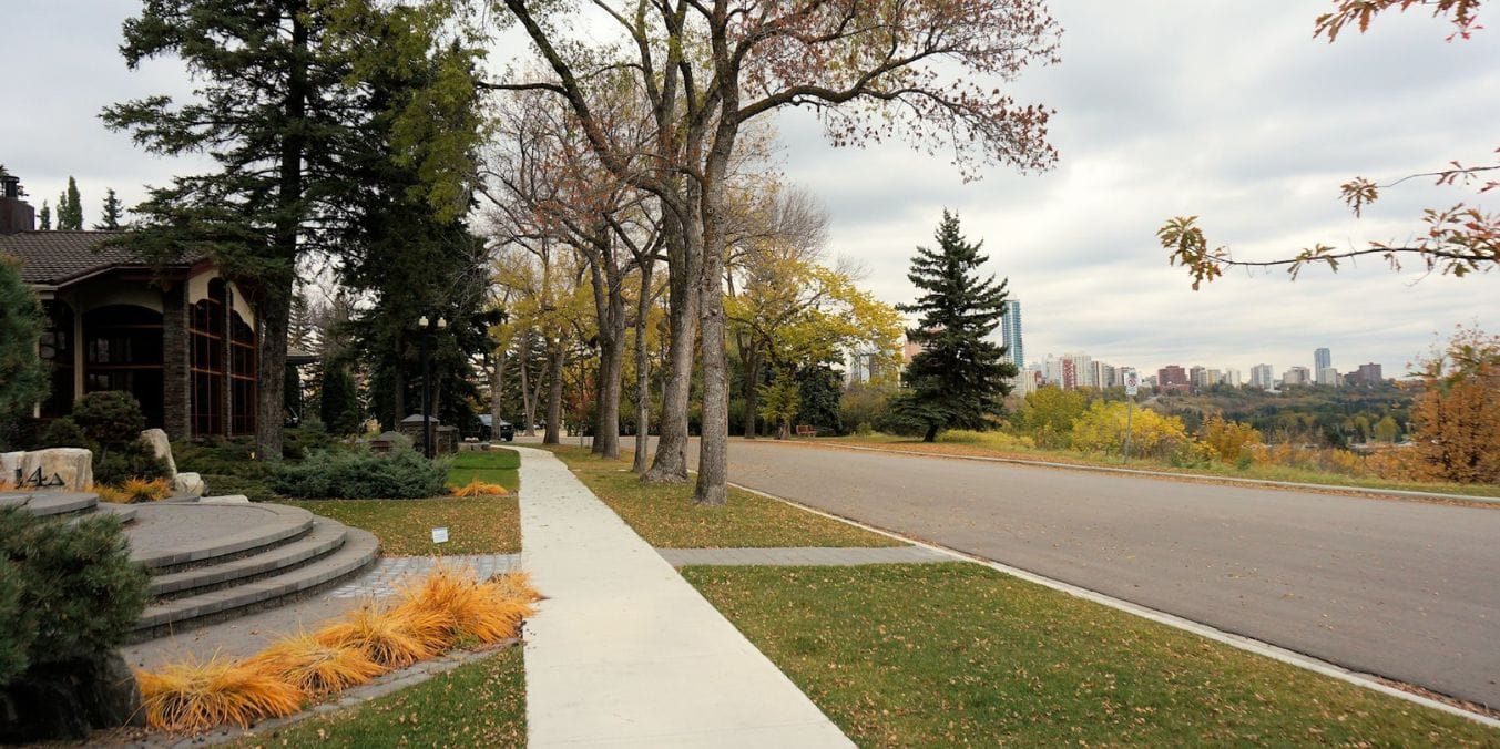 A serene street in Glenora, Edmonton, lined with trees and elegant homes, with a view of the city's skyline in the background, showcasing as one of the best neighborhoods.