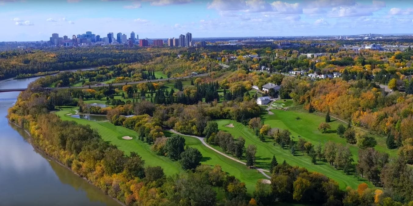 Aerial view of Highlands neighborhood in Edmonton, showcasing lush greenery, a golf course, and a mix of modern and heritage homes under a partly cloudy sky.