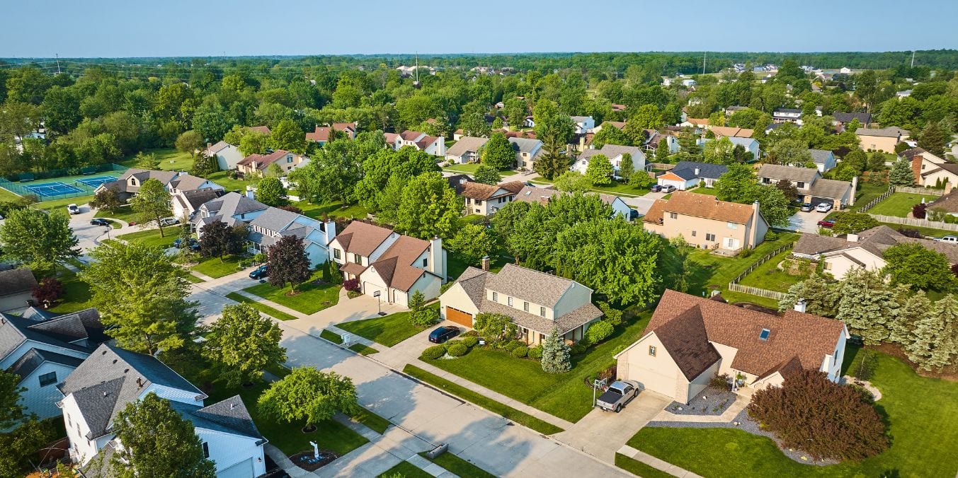 Aerial view of Westmount neighborhood, Edmonton, featuring tree-lined streets and homes with Mid-Century Modern and Ranch styles, under a clear blue sky.