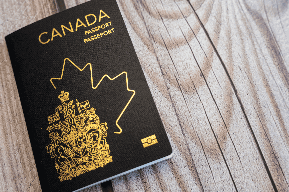 Canadian passport with gold emblem on a wooden surface, symbolizing travel and immigration to Canada.