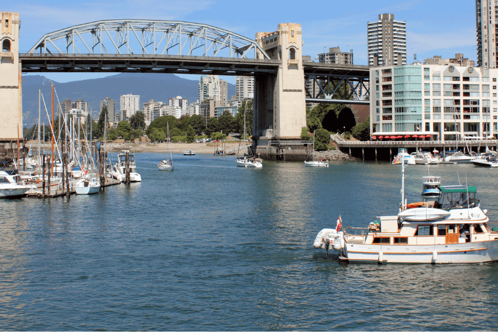 A scenic view of a waterfront area with boats docked and sailing, a bridge in the background, and city buildings, illustrating waterfront living and outdoor activities in a vibrant urban setting related to the British Columbia PNP Draw.