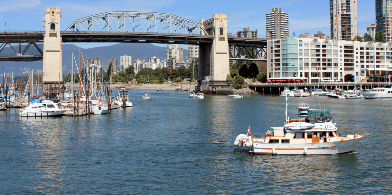 A scenic view of a waterfront area with boats docked and sailing, a bridge in the background, and city buildings, illustrating waterfront living and outdoor activities in a vibrant urban setting related to the British Columbia PNP Draw.