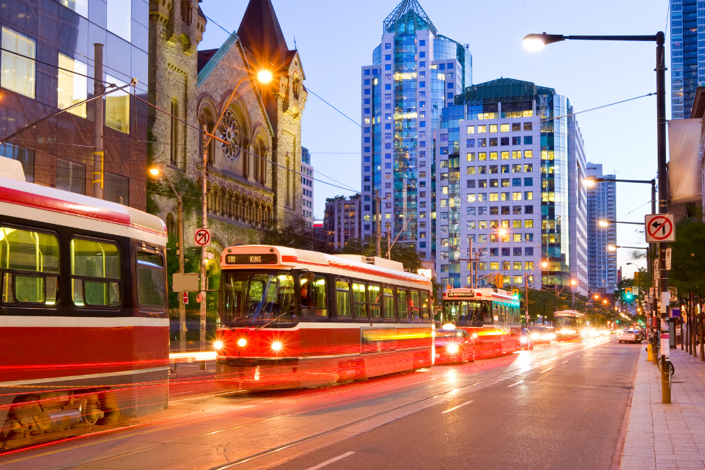 Toronto street at dusk with a red streetcar and city lights.