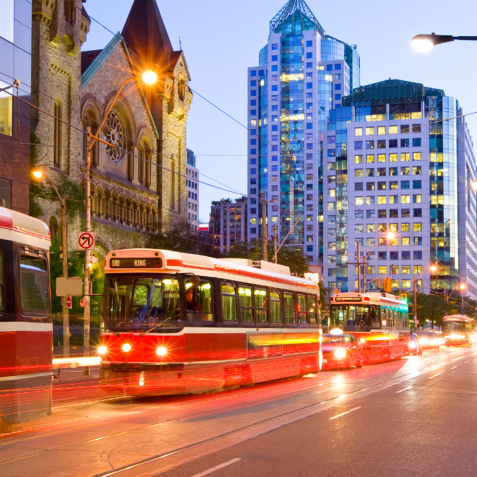 Toronto street at dusk with a red streetcar and city lights.