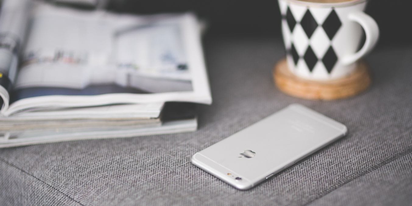 A sleek smartphone on a gray sofa, next to a stylish mug and an open magazine, representing lifestyle comparison in Montreal vs Toronto.