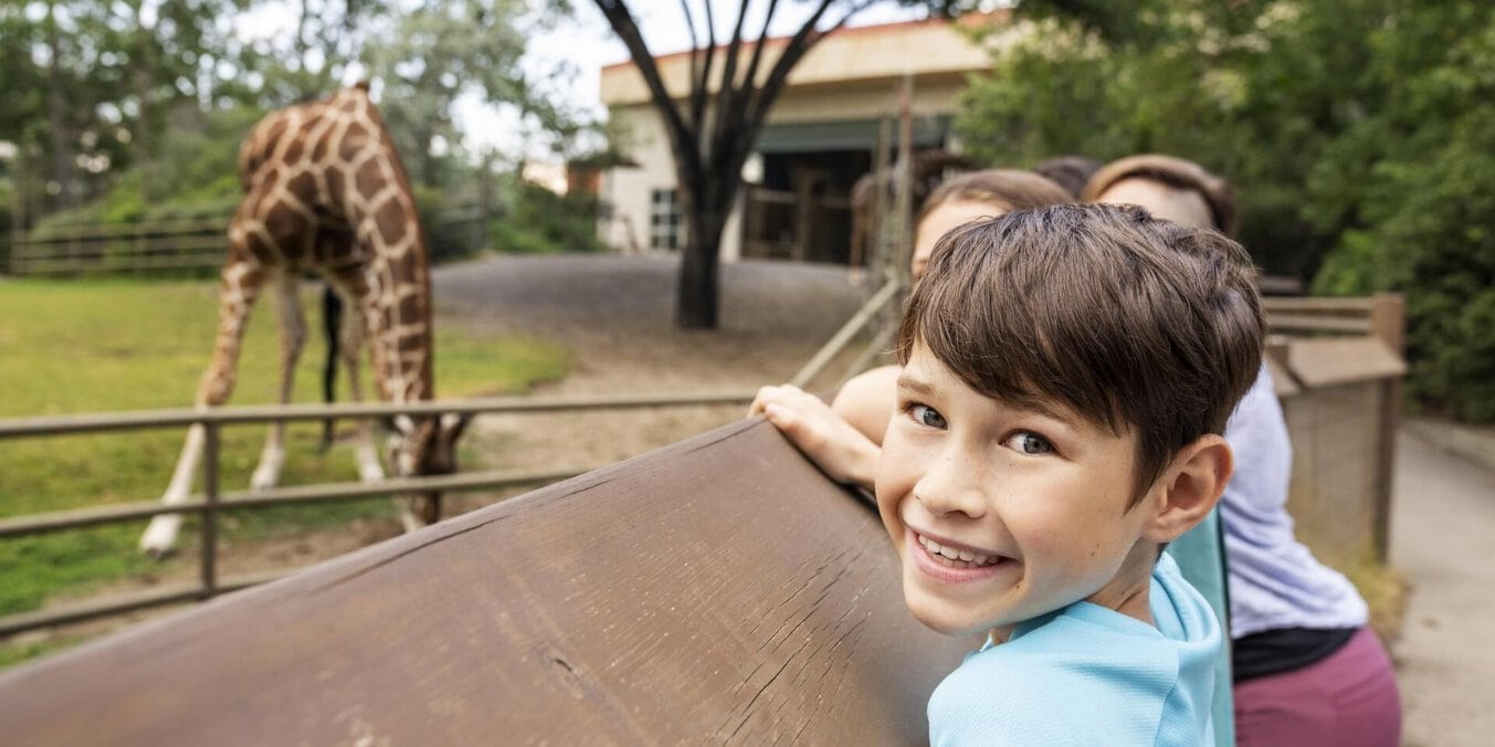 Child enjoying fun activities at Calgary Zoo with a giraffe in the background