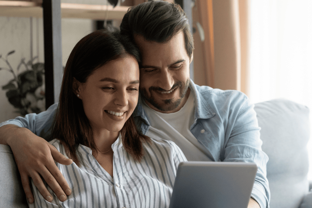 A happy couple researching how long spousal sponsorship takes in Canada on a tablet