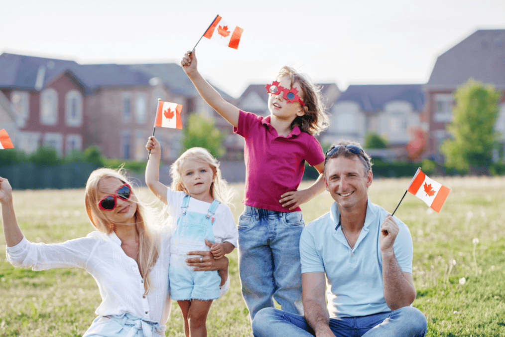 A happy family celebrates outdoors, waving Canadian flags. Discover the benefits of marrying a Canadian citizen and starting a life in Canada.