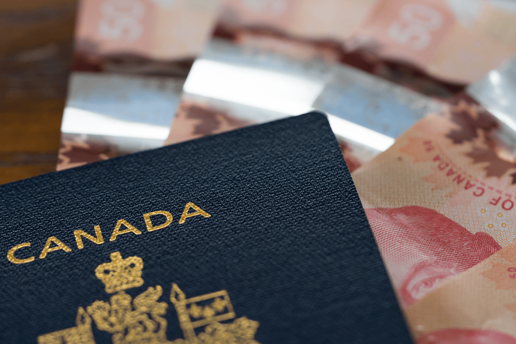 Close-up of a Canadian passport placed on a table with Canadian dollar bills in the background, symbolizing financial aspects of the Express Entry draw process for immigration.