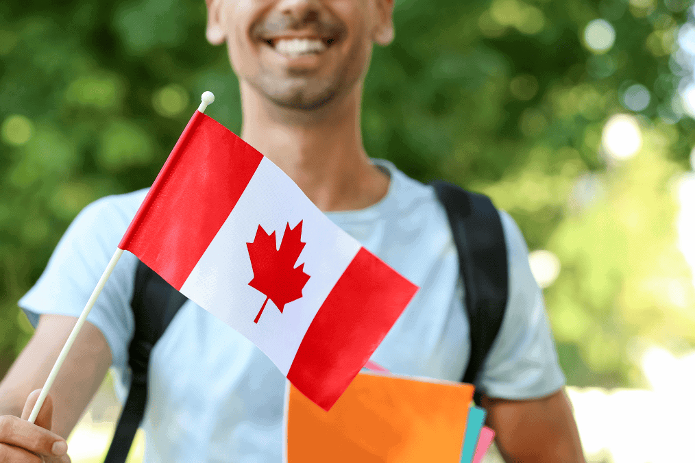 A smiling student holds a Canadian flag while carrying books, symbolizing their aspiration to obtain a study permit and pursue education in Canada.