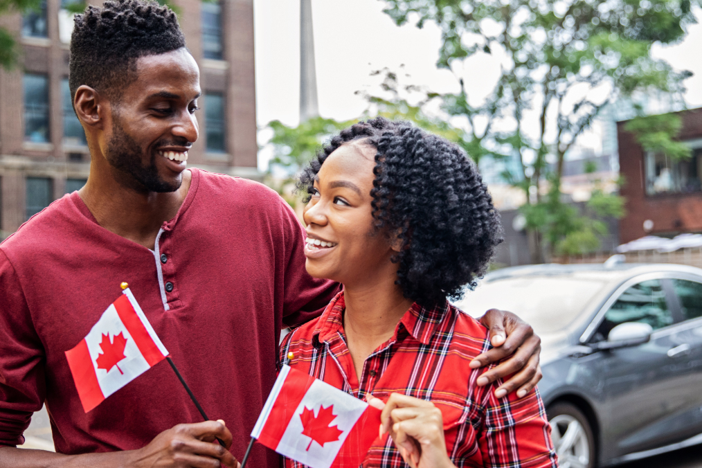 Is Calgary immigrant friendly? A happy couple holding Canadian flags smiles as they enjoy their new life in Calgary, showcasing the city's welcoming atmosphere and supportive environment for newcomers.