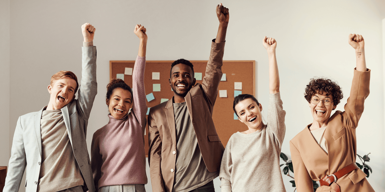 A diverse group of happy professionals celebrating together with raised arms, showcasing a positive work environment. This image reflects the social and work-life balance aspects when comparing life in Canada vs France.