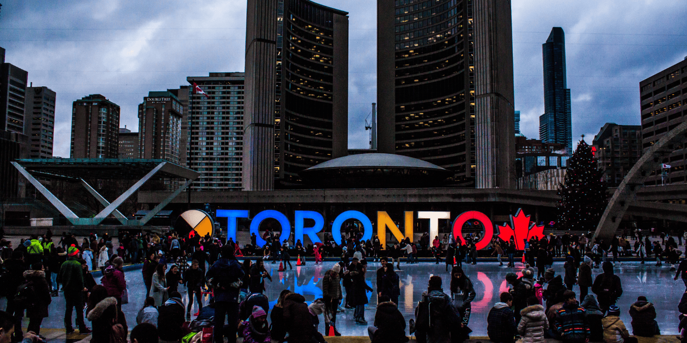 A bustling winter scene at Nathan Phillips Square in Toronto, with people ice skating in front of the brightly lit 