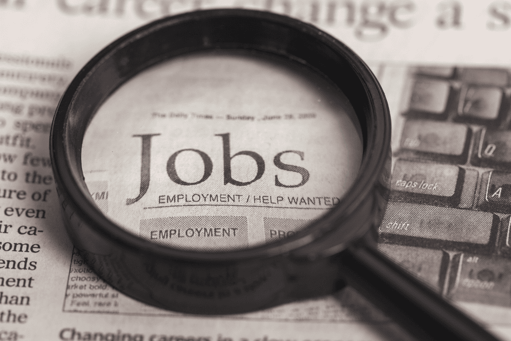 Magnifying glass over newspaper with the word 'Jobs' - Top 10 Highest Paying Jobs in Canada 2024