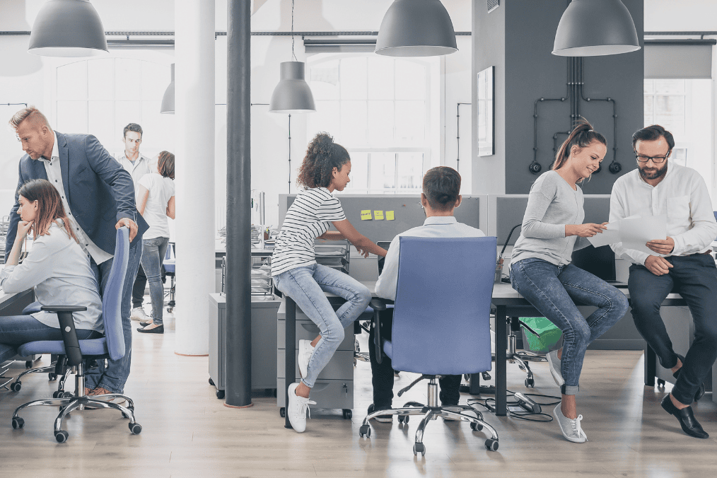 Modern office with people collaborating, discussing projects, and working at desks. Bright space, suitable for LMIA-exempt job roles.