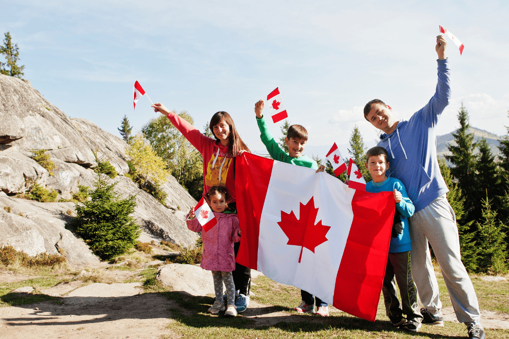 Family celebrating outdoors with Canadian flags, showcasing the advantages of Canadian citizenship.