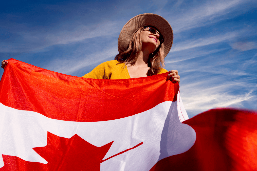 A woman proudly holding a Canadian flag under a bright blue sky, symbolizing the immigration process known as flagpoling in Canada.