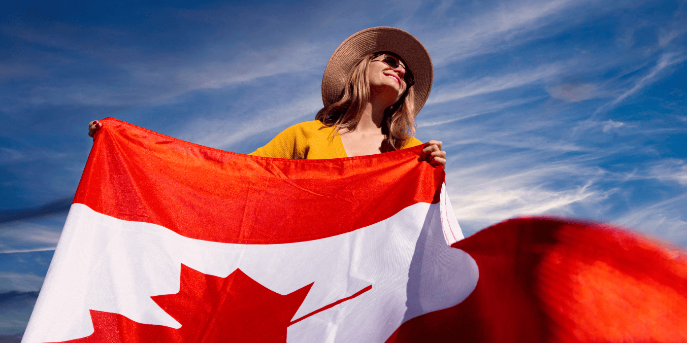 A woman proudly holding a Canadian flag under a bright blue sky, symbolizing the immigration process known as flagpoling in Canada.