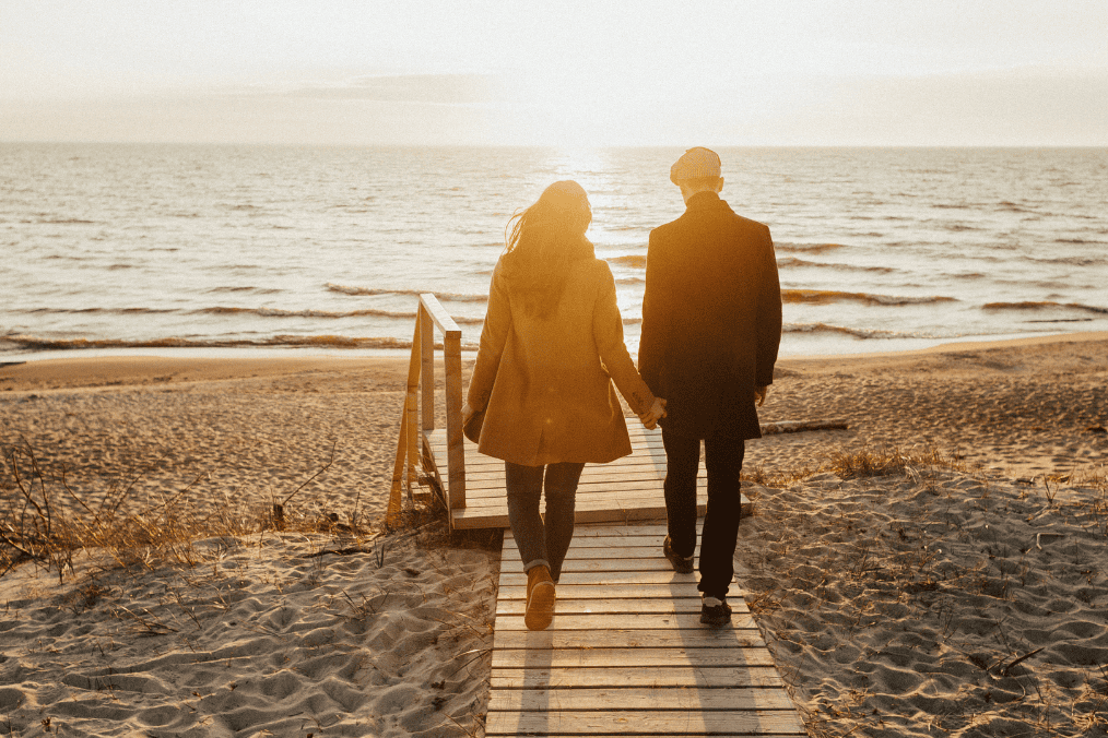 Can I sponsor my boyfriend to Canada? A couple holding hands, walking on a sandy beach towards the sunset, symbolizing a journey towards a new life together in Canada.