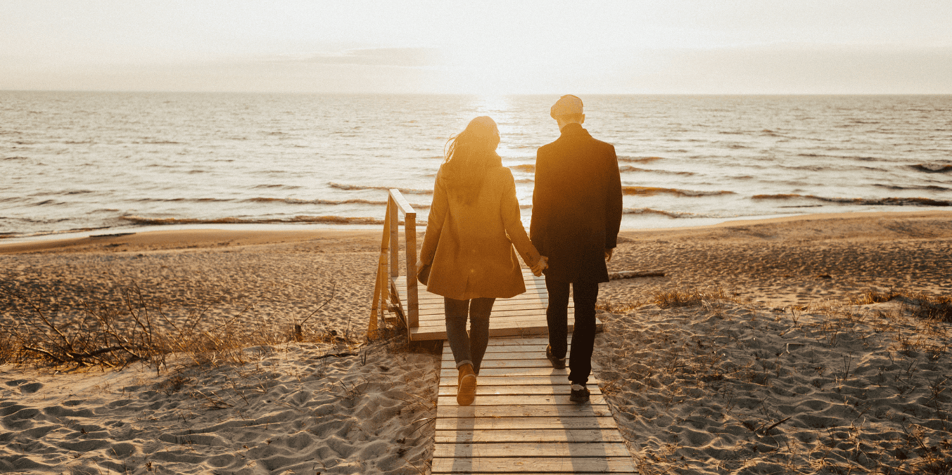 Can I sponsor my boyfriend to Canada? A couple holding hands, walking on a sandy beach towards the sunset, symbolizing a journey towards a new life together in Canada.