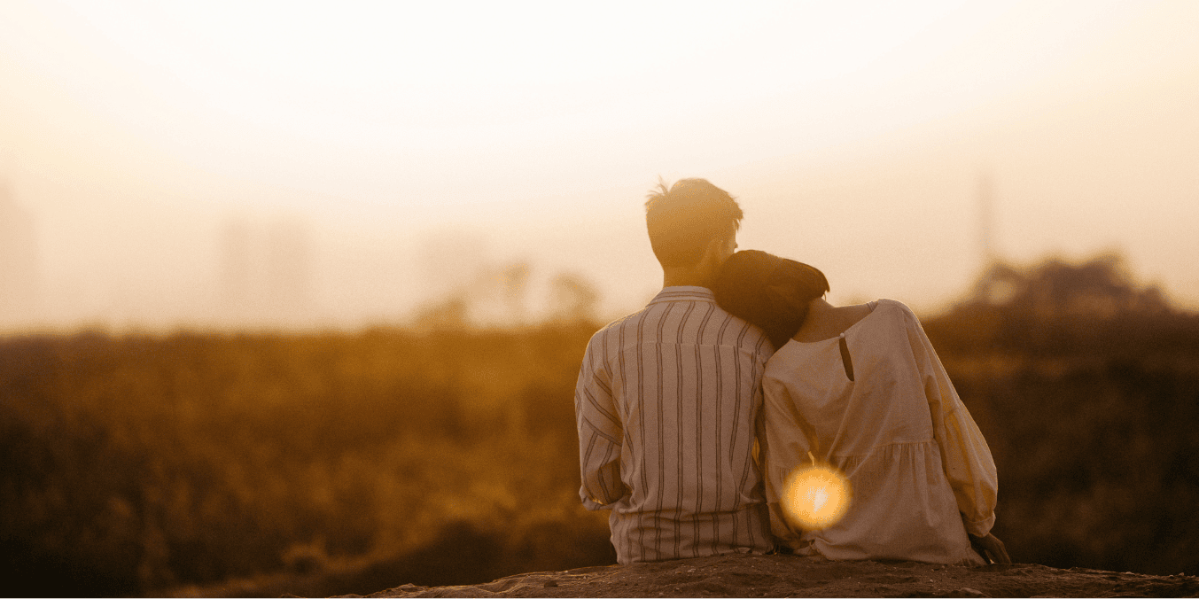 Can I sponsor my boyfriend to Canada? A couple sitting closely together, with the woman resting her head on the man's shoulder as they look out over a scenic, sunlit landscape, symbolizing the hope of building a life together in Canada.