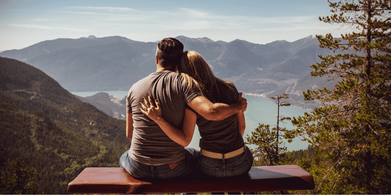 Can I sponsor my boyfriend to Canada? A couple sitting on a bench, embracing while overlooking a scenic mountain and lake view, symbolizing the dream of building a future together in Canada.