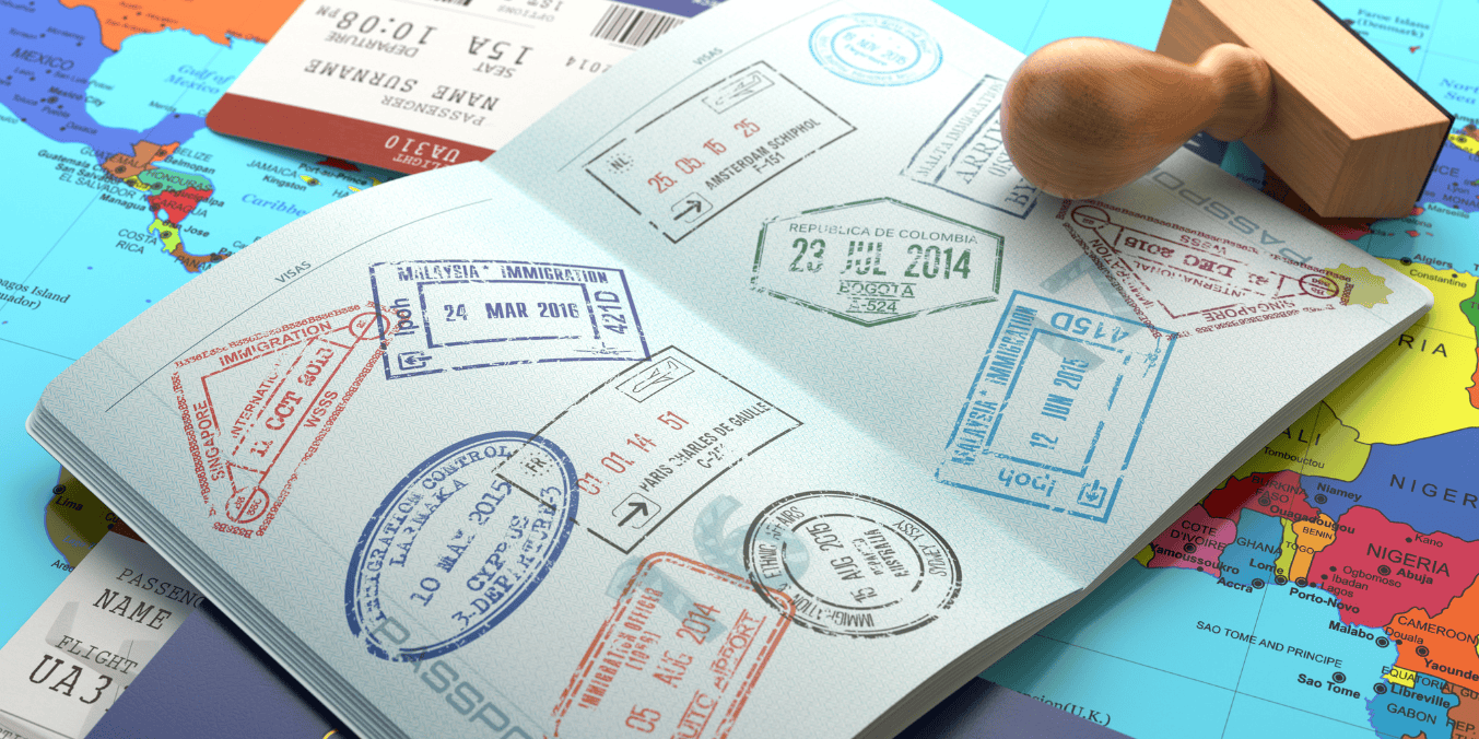 Open passport displaying various international visa stamps on a world map background, with a wooden stamp nearby.