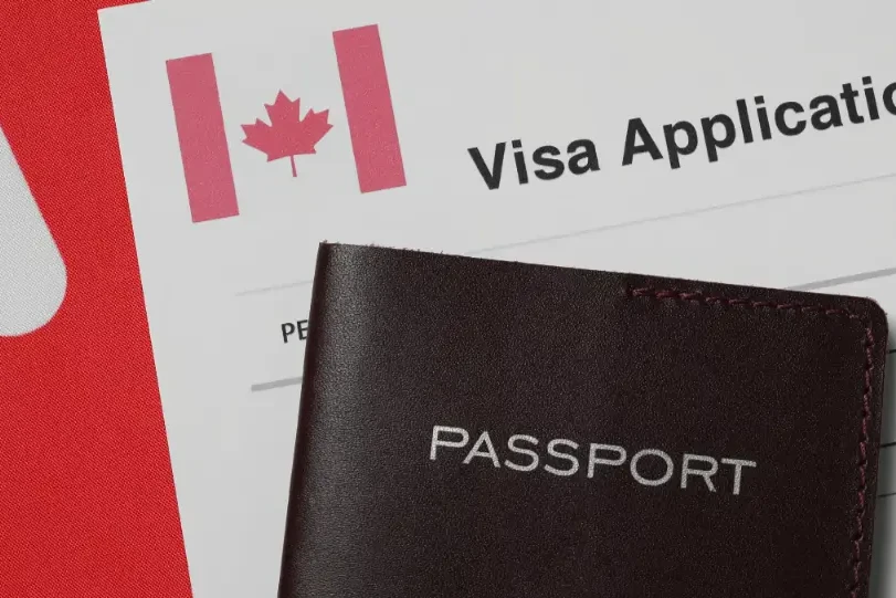 Temporary Resident Visa Canada application form with a passport placed on top, featuring a Canadian flag symbol.