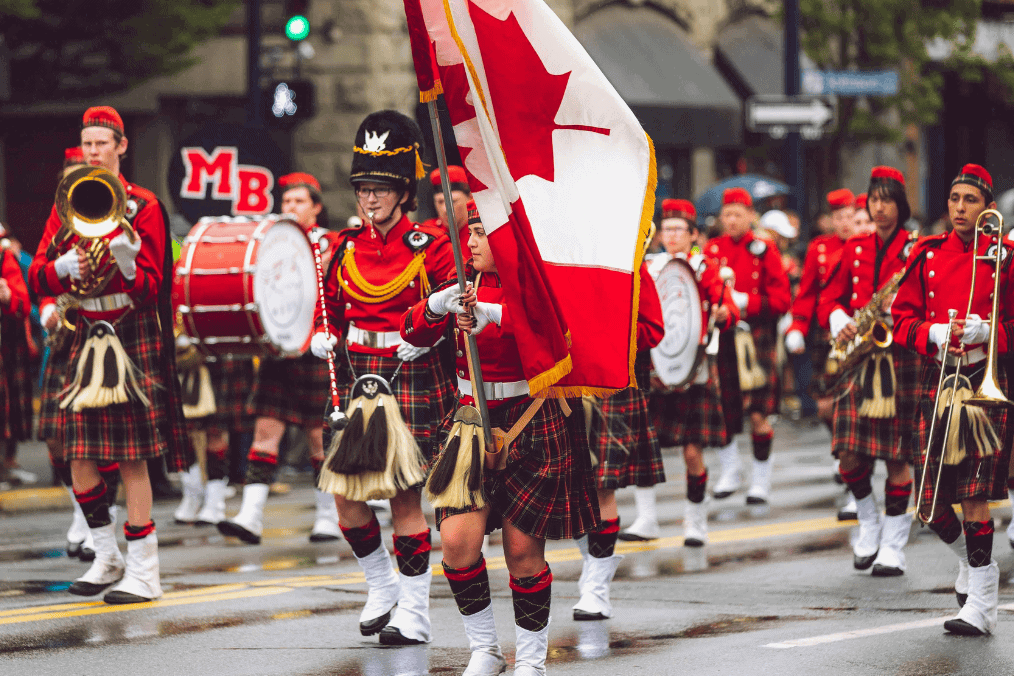 A marching band dressed in traditional red uniforms and tartan kilts parades down a rainy Canadian street, proudly displaying the Canadian flag, symbolizing the celebration of diversity and opportunities like the Express Entry Draw for immigration to Canada.