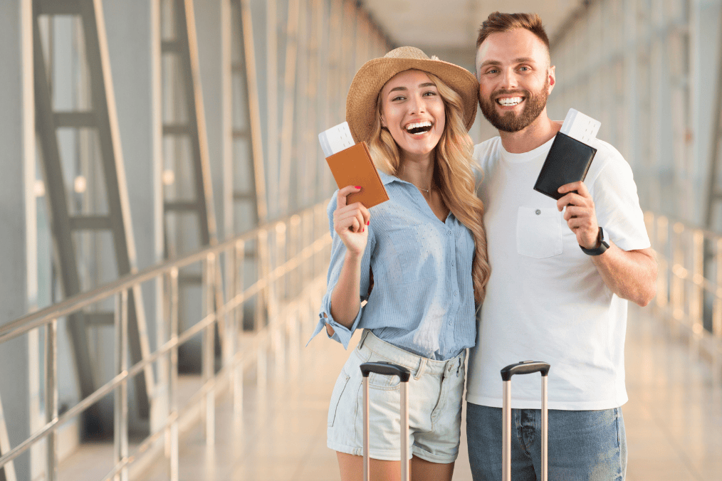 Happy couple at the airport holding passports and boarding passes, prepared to travel after learning how to renew Canadian passport for international trips.