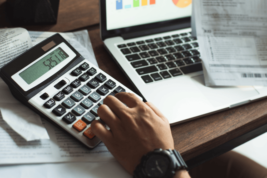 Calculating LMIA costs with a calculator, financial documents, and a laptop displaying charts – understanding how much does LMIA cost.