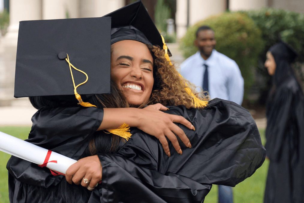 Two graduates celebrating in caps and gowns, holding a diploma, on graduation day—ready to meet PGWP requirements for work in Canada.